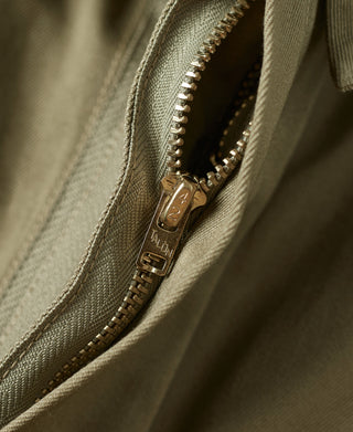Khaki green jacket zipper close-up with metal pull and tan stitch trim