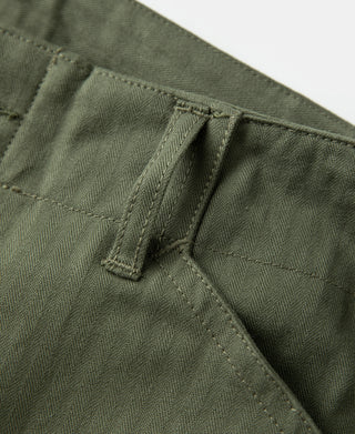 Olive pants pleat and pocket corner close-up with bar-tack stitching.