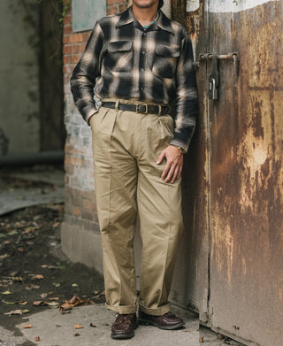 Khaki double-pleat cotton twill trousers on model with belt and cuffed hem