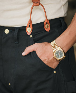 Navy canvas pants with leather suspender straps, snap buttons, and front pockets